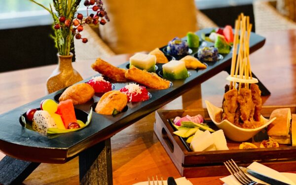 high tea set, with satay (grilled chicken) with sliced onion, nasi impit, cut fruits such as dragon fruit, watermelon, grapes and more. Enjoy Malay kuih on a congkak board