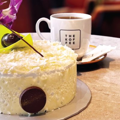 image features Pistachio perfection cake (Pistachio White Forest Cake) and a cup of coffee on the side