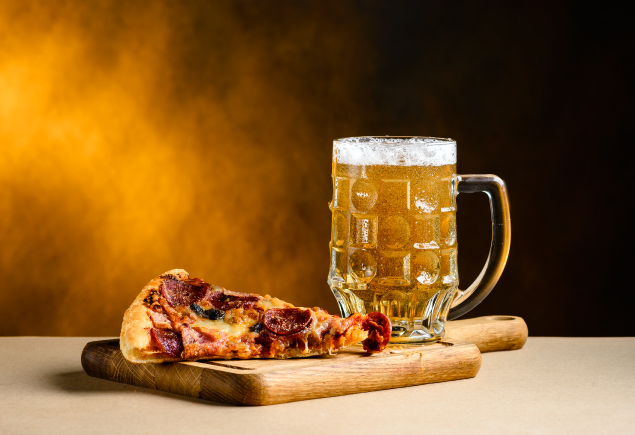 The photo shows a slice of pizza and a mug of beer.