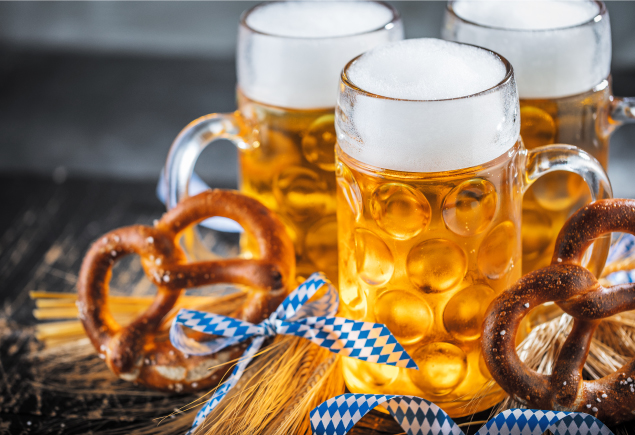 Three mugs of beer with two pretzels and some decoration son the table.
