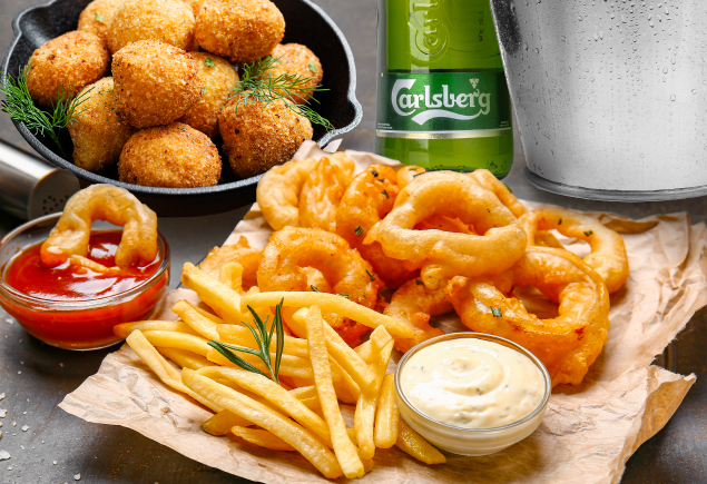 A plate of onion rings, french fries and potato croquettes along with a bucket of beer are placed on the table.
