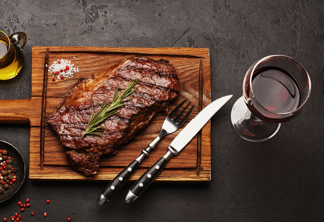 The photo shows a steak with a glass of red wine.