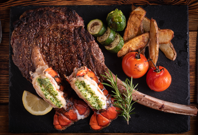 Australian Black Angus Tomahawk and Grilled Lobsters with tomatoes, wedges, cucumbers and a slice of lemon on the side.