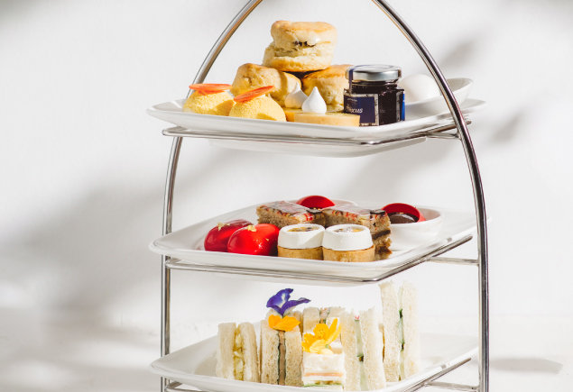 The photo shows a high tea set with three tier of baked goods and desserts.