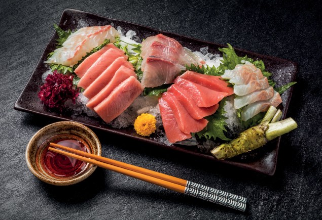Five types of sliced sashimi on a plate with chopstick and soy sauce at the side.