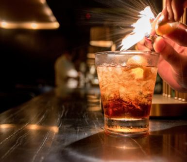A glass of cocktail. The mixologist is lighting fire to the cocktail for presentation.