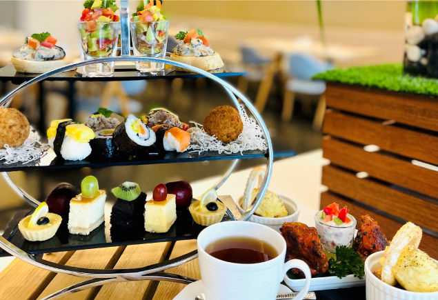 High tea set consisting of sushi, sandwich, desserts and with a cup of tea.