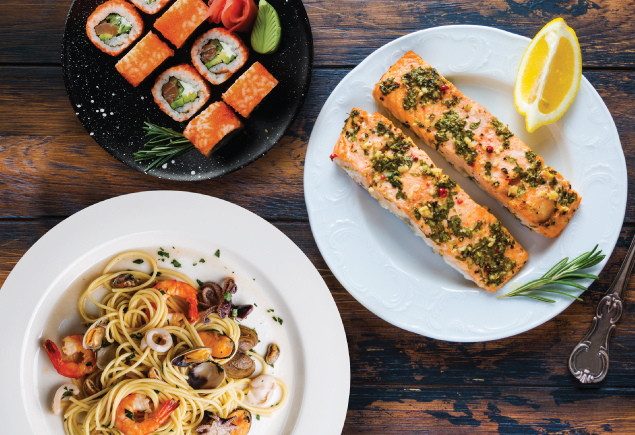 Three plates of food are placed on the table. Eight pieces of California roll sushi, Two slices of slow roasted salmon fillet and seafood aglio olio spaghetti.
