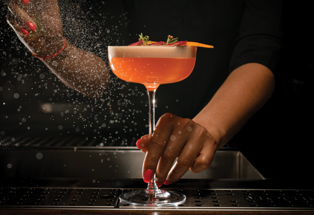 A mixologist is serving a glass of cocktail.