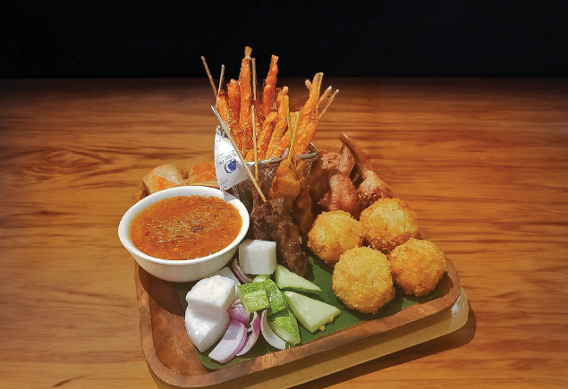 A snack platter. It has fries, fried potato balls, satay with condiments and fried chicken.
