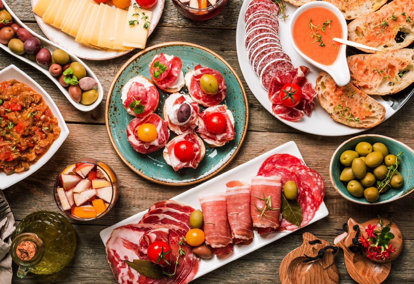 A vairety of cold cuts and tapas dishes with a glass of sangria are on the table.