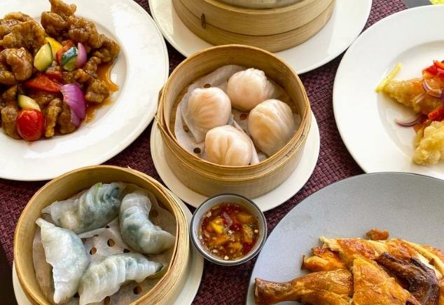 A variety of Chinese food such as Sweet and Sour Chicken, Har Gow, Steamed Dumplings and Fried Chicken are on the table.
