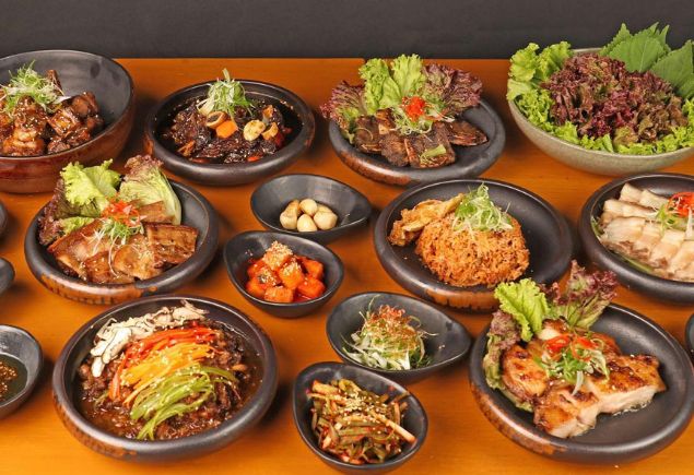Nine variety dishes of Korean food and four small plates of side Korean dishes on the table.