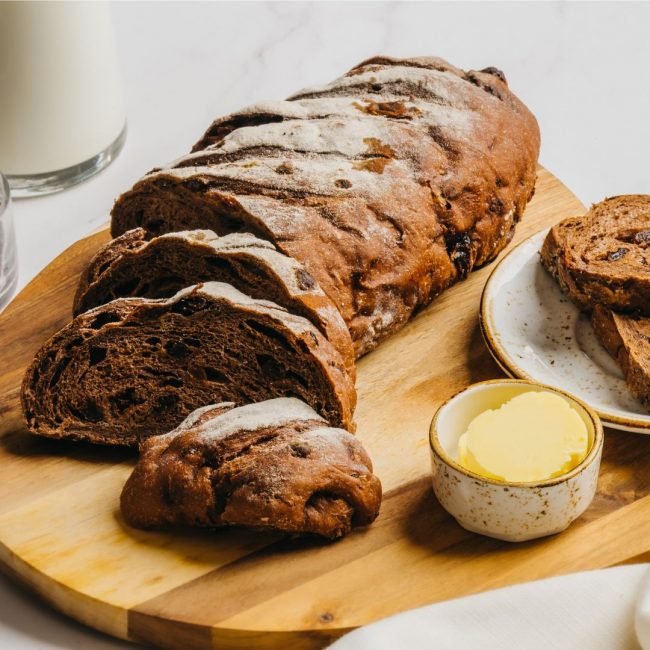 A loaf of sliced Chocolate Raisin Sourdough bread with butter on the side.