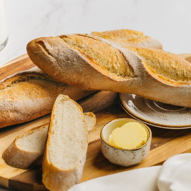 The photo shows a loaf and slices of Baguette with butter on the side.