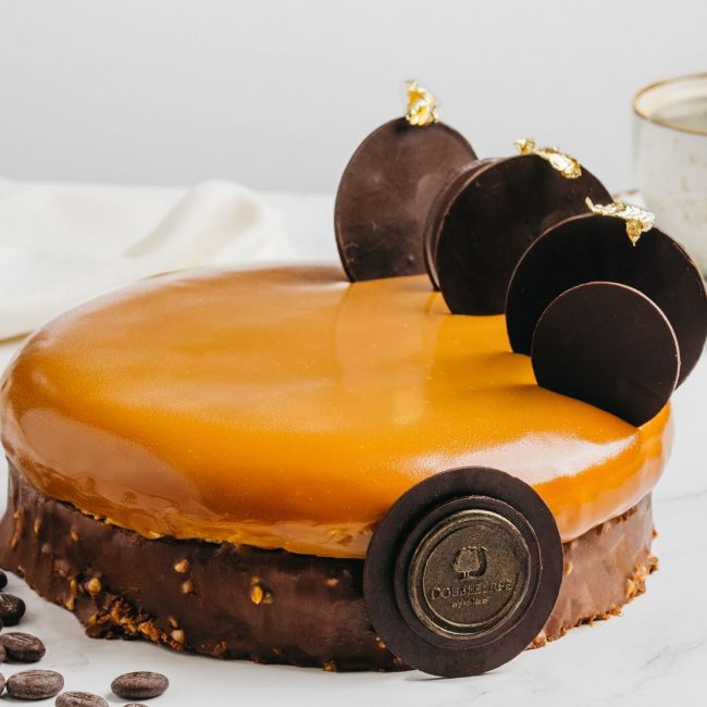 A whole cake of Coffee Caramel Mousse cake decorated with chocolate pieces.