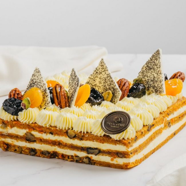 A whole cake of Carrot cake with a variety of chocolates and fruits and cream on top.