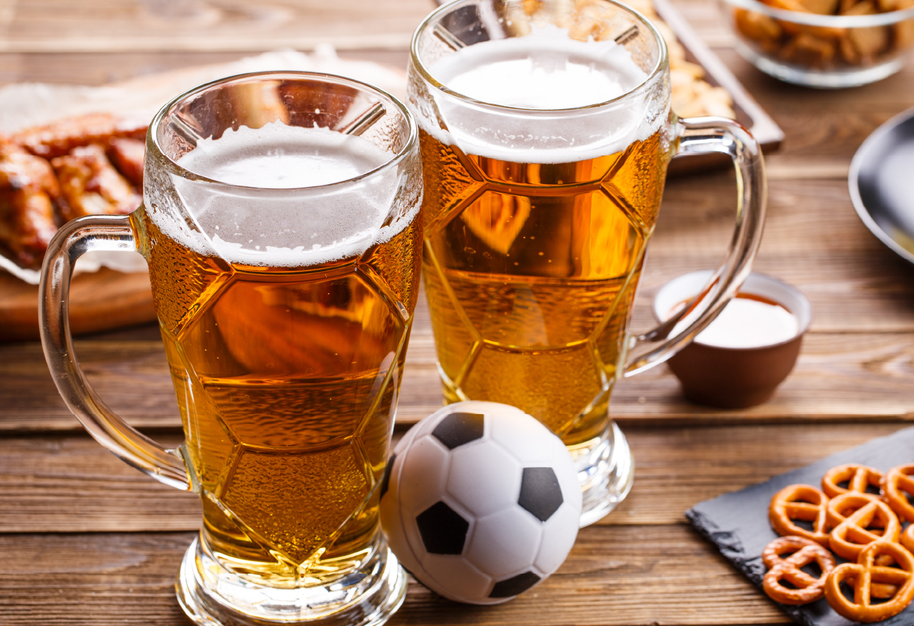 The photo shows two cups of beer with a mini football plushie in front.
