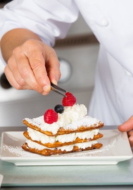 A pastry chef is placing berries on top of the strudel