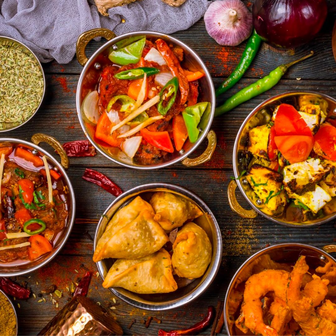 Five plates of various Indian dishes are placed on the table along with the ingredients used.