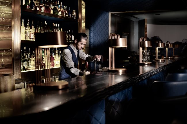 A mixologist is mixing up a cocktail drink behind the bar table at Hilton Kota Kinabalu's The Club