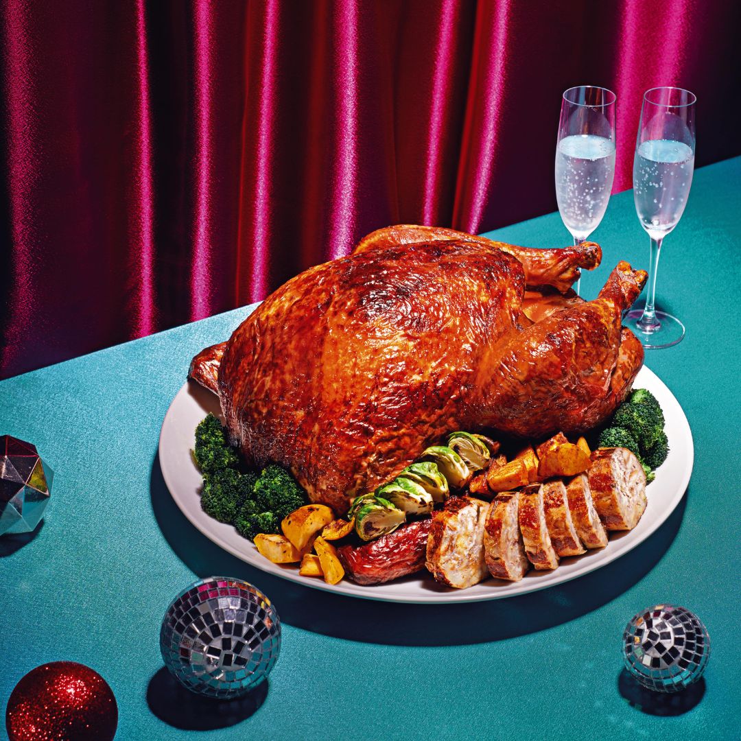 A whole turkey with stuffing vegetables, potatoes and sliced meat. Two glasses of sparkling water is placed at the side.