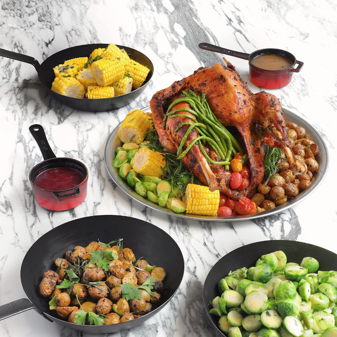 The photo shows a few festive dishes such as a whole turkey with potatoes, brussels sprout, corns and tomatoes. Two types of sauces are place at the side.