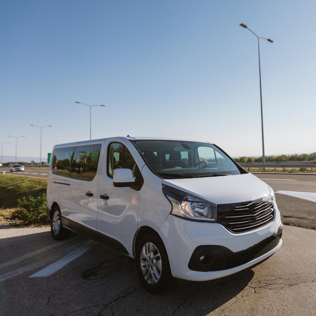 A white van is parked on the side of the highway. The background shows a clear bue sky, a highway, a few highway light poles and grasses.