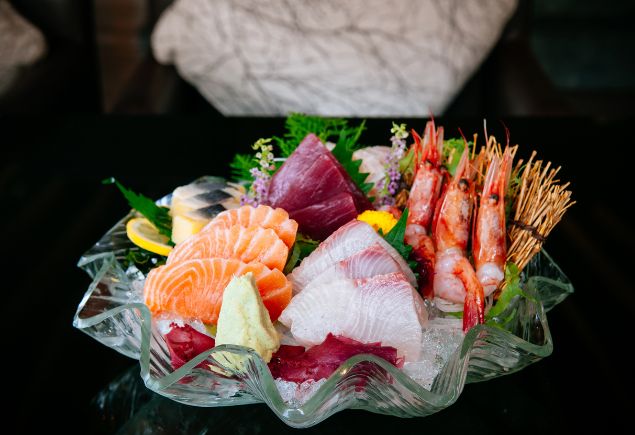 A bowl full of fresh sashimi such as sliced salmon, sliced tuna, prawns and sliced yellowtail.