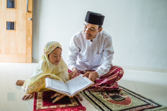 A Muslim father and daughter are reading prayers together.