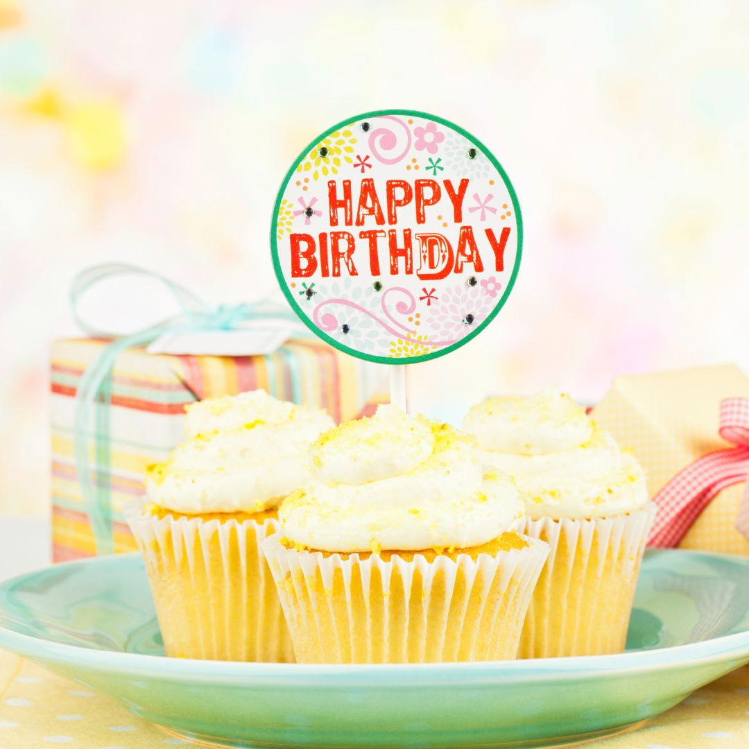 Three vanilla flavoured cupcakes are on a light blue plate. On top of the middle cupcake, it has a "Happy Birthday" signage.
