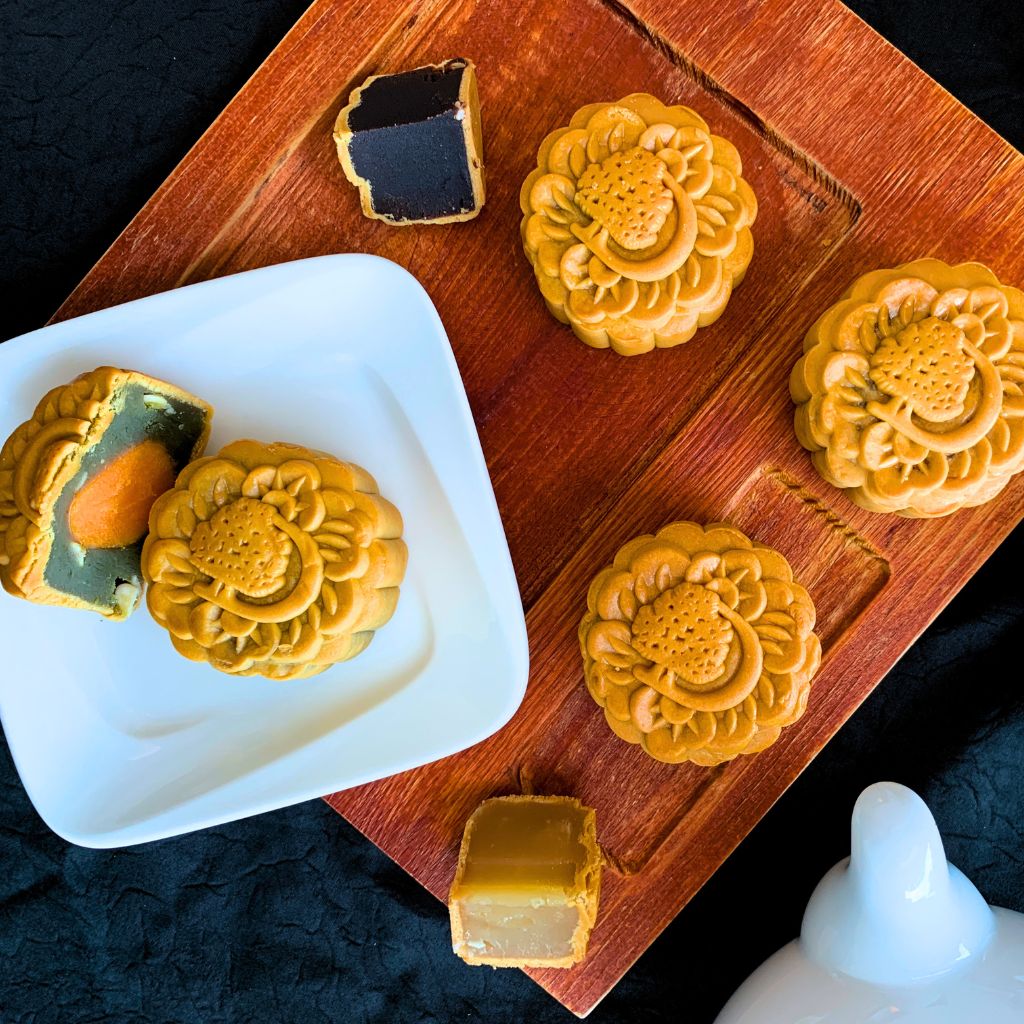 A variety of baked mooncakes is available, with some of them being cut into halves to showcase different flavors.