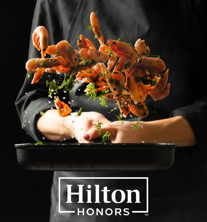 Chef in black uniform tossing prawns in a skillet pan